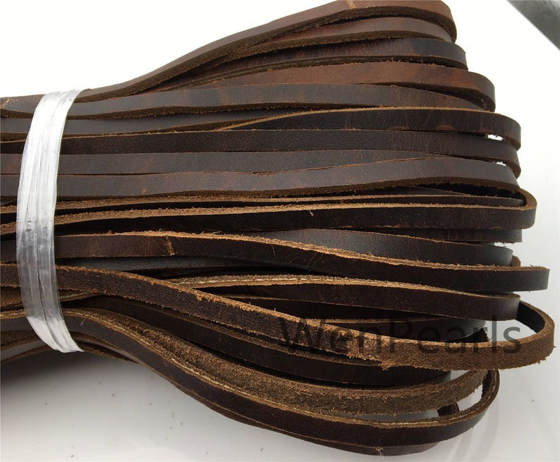 Op de afbeelding: Een bundel bruin lederen koord, ongeveer 6 mm breed, is samen gewikkeld met een doorzichtig plastic band. Het lederen koord is zacht en soepel, en het is perfect voor knutselprojecten.