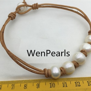 May include: A brown leather bracelet with five white pearls and a knot at each end. The bracelet is approximately 11 inches long. WenPearls is written on the white background.