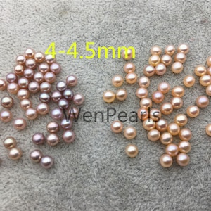 May include: A pile of approximately 40 small, round, pink and purple freshwater pearls, measuring 4-4.5 mm in diameter. The pearls are scattered on a light brown, textured surface. The text "4-4.5mm" is written in yellow above the pearls.