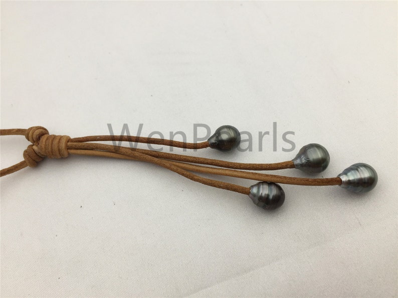 May include: A brown leather cord necklace with five dark gray pearls hanging from it. The cord is knotted at the top and the pearls are evenly spaced.