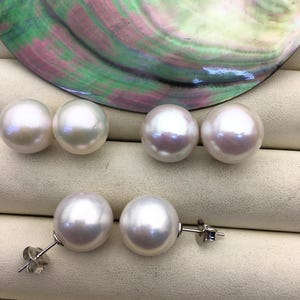 May include: A set of three pairs of white pearl earrings. The earrings are displayed on a white surface with a mother-of-pearl shell in the background.