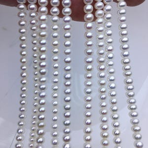 Puede incluir: Una hebra de perlas de agua dulce blancas, enhebradas en un hilo fino. Las perlas son redondas y lisas, con un ligero brillo iridiscente.