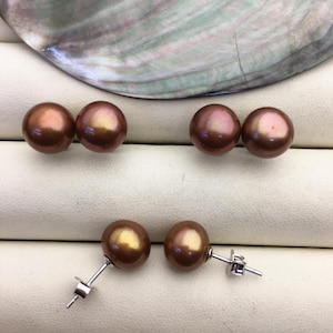 May include: Three pairs of brown pearl earrings with silver posts. The pearls are round and have a slight iridescent sheen.