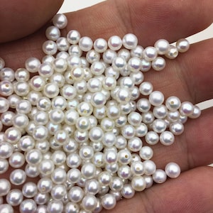 May include: A large pile of white round pearls with a slight iridescent sheen. The pearls are smooth and have a hole drilled through the center.