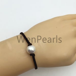 Peut inclure: Un bracelet en perle blanche avec un cordon noir. Le bracelet est noué et la perle est centrée sur le cordon.
