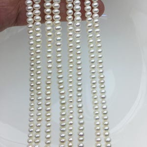 May include: Multiple strands of white pearls are shown, each with a uniform size and shape, set against a white backdrop. The pearls are strung together, giving a delicate and elegant look. The image emphasizes the lustre and consistency of the pearls.