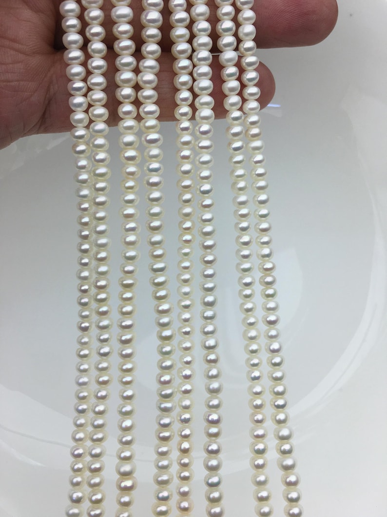 May include: Multiple strands of white pearls are shown, each with a uniform size and shape, set against a white backdrop. The pearls are strung together, giving a delicate and elegant look. The image emphasizes the lustre and consistency of the pearls.