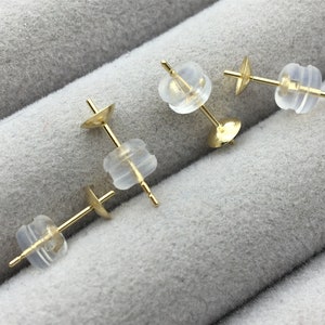 May include: Three gold earring backs with clear rubber stoppers. The earring backs are designed to secure earrings to the earlobe.