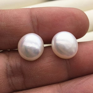 Puede incluir: Dos perlas blancas de forma ovalada, cada una con una superficie lisa y brillante.