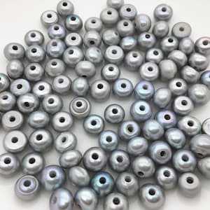 Puede incluir: Un montón grande de cuentas de perlas grises con un agujero en el centro de cada cuenta. Las cuentas son redondas y tienen un ligero brillo iridiscente.