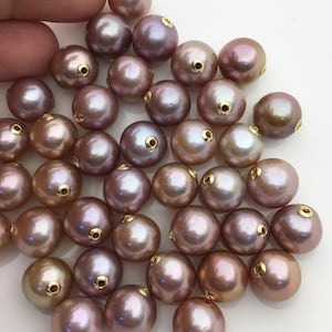 Puede incluir: Un montón de perlas redondas, iridiscentes, de color púrpura claro con tapas de metal dorado. Las perlas tienen un diámetro aproximado de 10 mm.