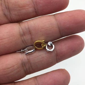 Pu&ograve; includere: Primo piano di tre piccole chiusure per gioielli in tonalit&agrave; argento e oro. Le chiusure sono in diversi stili, tra cui un moschettone, una forma a ferro di cavallo e una chiusura rotonda con una piccola pietra trasparente. Le chiusure sono tenute in una mano.
