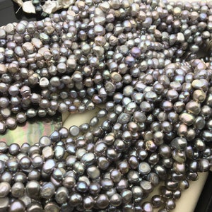 May include: A strand of grey freshwater pearls. The pearls are irregular in shape and have a slight iridescent sheen.