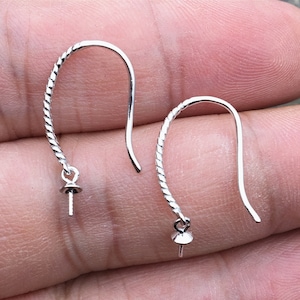 May include: Two silver-colored earring hooks with a twisted design on the lower portion. Each hook has a small, round component with a post extending downwards, likely for attaching beads or other decorative elements. The hooks are curved and appear to be made of metal.
