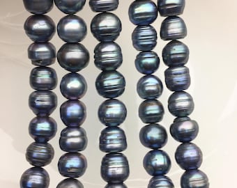 Puede incluir: Una hebra de perlas de agua dulce de color gris oscuro con matices iridiscentes azules y verdes. Las perlas son redondas y lisas, y están enhebradas en un hilo transparente.