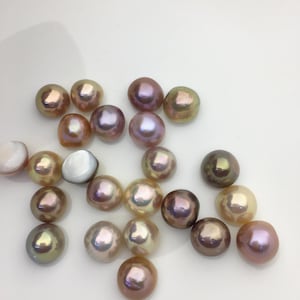 May include: A collection of iridescent pearls in various colors, including pink, gold, and purple. The pearls have a smooth, lustrous surface and are scattered on a white background. The pearls vary in size and shape, showcasing natural beauty.