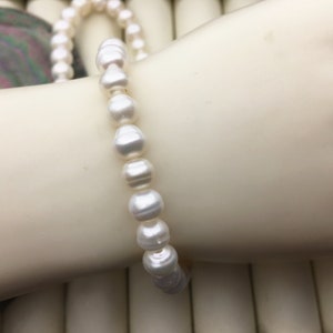 May include: A white pearl bracelet with a simple design. The bracelet is made of small, round pearls that are strung together on a thin, white cord.
