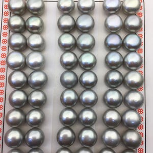 May include: A collection of grey pearls, each with a smooth, spherical form, arranged in neat rows. The pearls have a subtle sheen. The words "High Fashion" are printed at the top. These pearls are suitable for jewelry making.