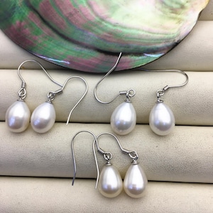 Può includere: Tre paia di orecchini a goccia di perla bianca con ganci d'argento. Le perle hanno una forma a goccia e una finitura liscia e lucida.