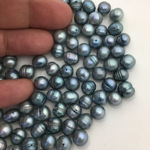 Könnte beinhalten: Ein Haufen blauer Süßwasserperlen, jede mit einem leicht schimmernden Glanz. Die Perlen sind rund und glatt und in einem zufälligen Muster angeordnet.