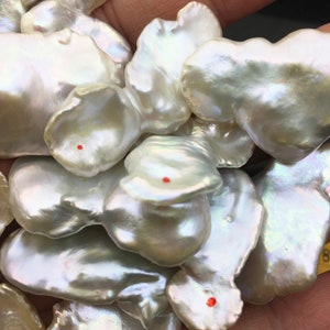 Pode incluir: Um close-up de um monte de p&eacute;rolas barrocas brancas. As p&eacute;rolas t&ecirc;m uma forma irregular e uma superf&iacute;cie lisa e iridescente.