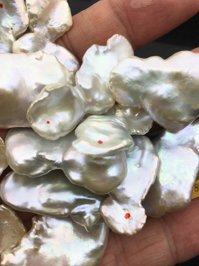 Pode incluir: Um close-up de um monte de p&eacute;rolas barrocas brancas. As p&eacute;rolas t&ecirc;m uma forma irregular e uma superf&iacute;cie lisa e iridescente.