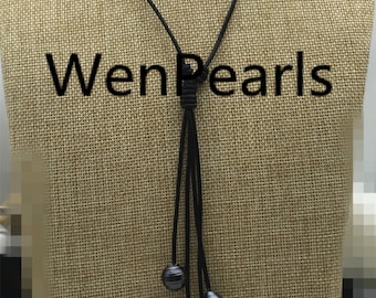 May include: A black leather cord necklace with four black pearls hanging from the bottom. The necklace is on a tan fabric background. The text "WenPearls" is visible in the image.