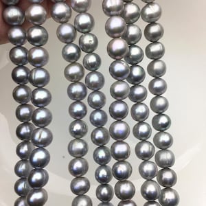May include: A strand of gray pearls with iridescent shimmer. The pearls are round and smooth, and they are strung on a clear thread.