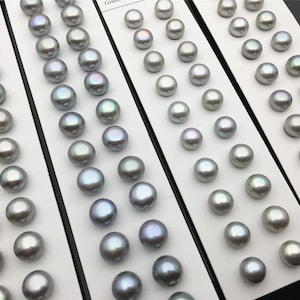 May include: A collection of 60 round, iridescent gray pearls arranged in rows on a white card. The pearls are approximately 10mm in diameter.