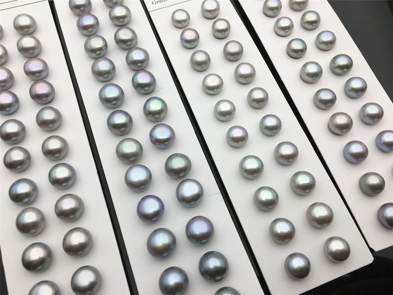 May include: A collection of 60 round, iridescent gray pearls arranged in rows on a white card. The pearls are approximately 10mm in diameter.