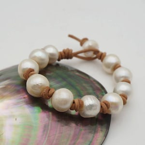 May include: A white pearl bracelet with a brown leather cord. The bracelet is tied with a knot and has a simple design.