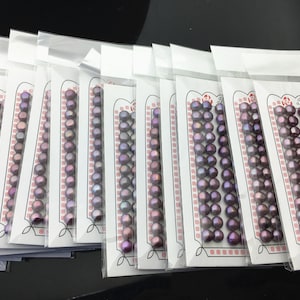 Pode incluir: Múltiplos pacotes de pérolas de água doce roxas, cada um contendo um fio de pérolas. Os pacotes são etiquetados como "High Fashion".