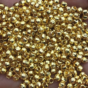 May include: A large pile of gold-colored metal beads. The beads are round and have a faceted design.