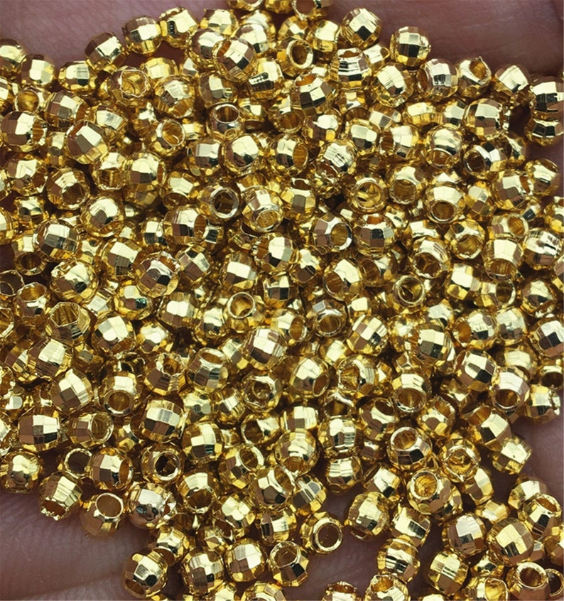 以下が含まれることがあります： 金色の金属ビーズがたくさん入った山。ビーズは丸く、ファセットカットが施されています。