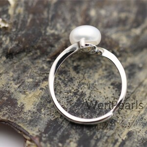 May include: A silver ring with a white pearl set on top. The ring is on a dark brown surface with the text "WenPearls" visible.