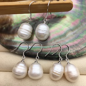 Può includere: Un paio di orecchini pendenti con perle bianche e ganci d'argento. Le perle sono di forma ovale e hanno una finitura liscia e lucida.