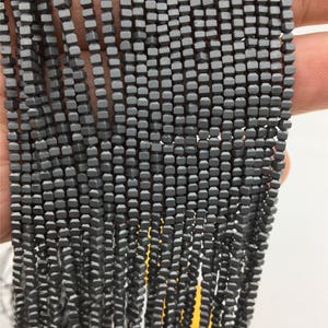 May include: A strand of dark gray square-shaped beads. The beads are strung on a thin wire and are all the same size.