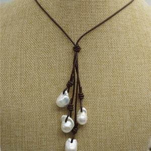 Puede incluir: Un collar de cuero marr&oacute;n con un dise&ntilde;o anudado y cinco perlas barrocas blancas que cuelgan de la parte inferior.