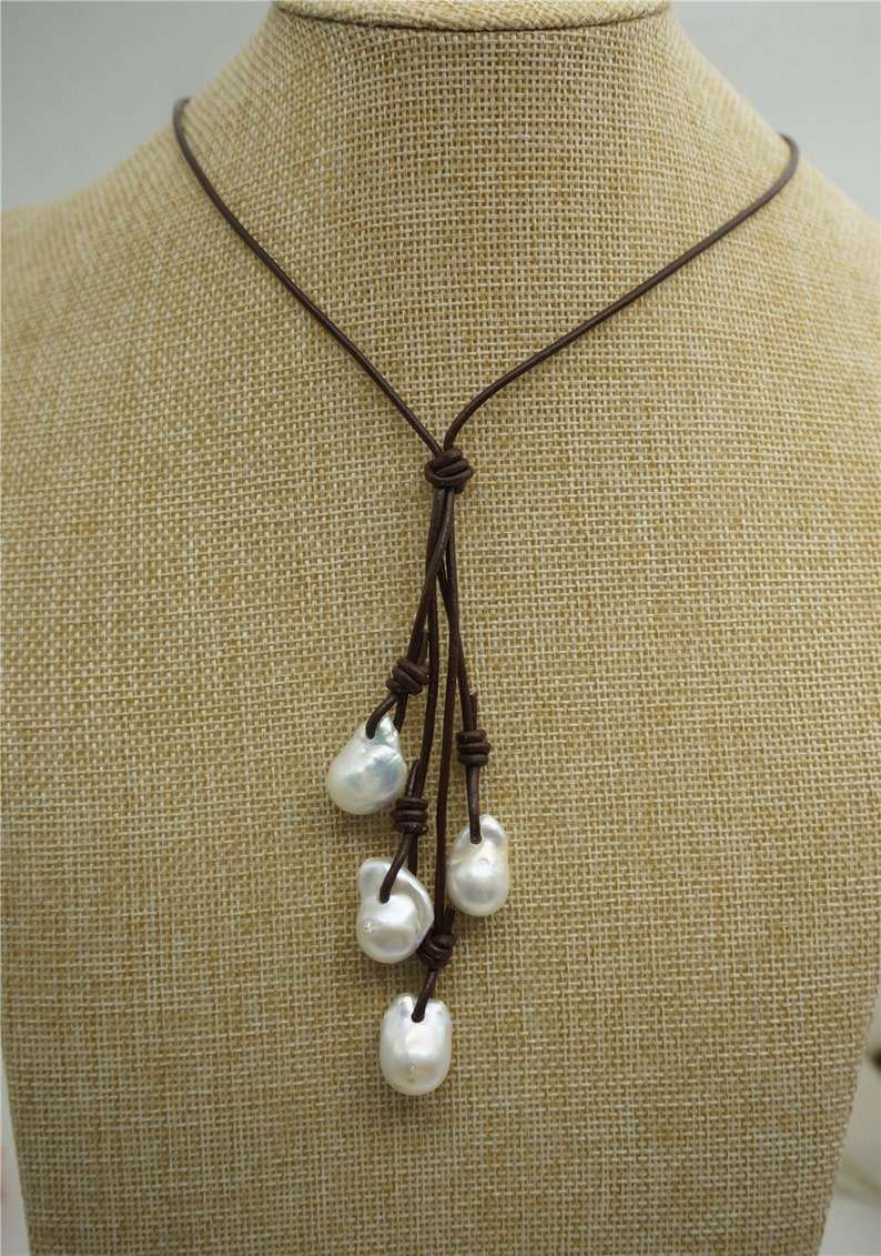 Puede incluir: Un collar de cuero marr&oacute;n con un dise&ntilde;o anudado y cinco perlas barrocas blancas que cuelgan de la parte inferior.