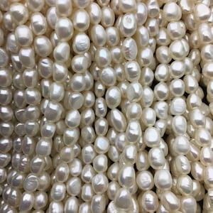 May include: A close-up of a pile of white, off-white, and cream-colored baroque pearls. The pearls are smooth and have a slight iridescent sheen.