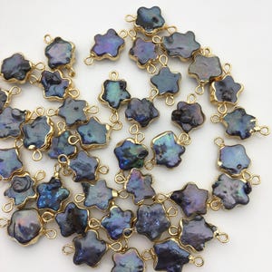 May include: A collection of dark blue, irregularly shaped pearl pendants with gold-coloured metal edging and loops. The pearls have iridescent qualities, reflecting shades of purple, green, and blue. These pendants are ideal for jewellery making.