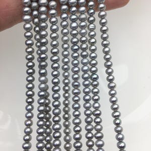 May include: Multiple strands of small, round, light gray pearls arranged in vertical lines. Each strand consists of numerous individual pearls with a smooth, lustrous finish, creating a uniform and consistent appearance across the collection.