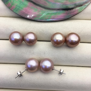 May include: Three pairs of pink pearl earrings. The pearls have a lustrous sheen and are set on silver posts. The background features a decorative shell with iridescent colors.