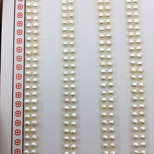 Puede incluir: Cuatro filas de perlas blancas dispuestas verticalmente sobre un fondo blanco. Cada fila contiene 20 perlas.