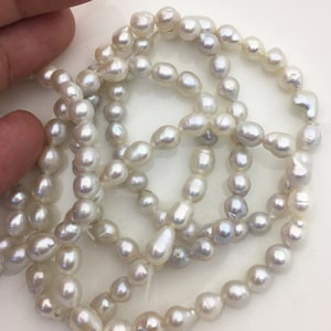 Könnte beinhalten: Eine Strähne weißer Süßwasserperlen mit leicht unregelmäßiger Form, perfekt für die Schmuckherstellung.