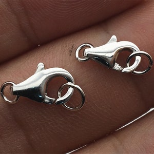 Puede incluir: Dos cierres de langosta plateados con un anillo redondo unido a cada uno. Los cierres están abiertos y listos para ser unidos a una cadena o cordón.