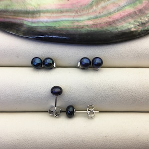 Op de afbeelding: Een paar zwarte parel oorbelletjes met zilveren pinnen en achterkanten. De oorbelletjes worden getoond op een wit oppervlak.