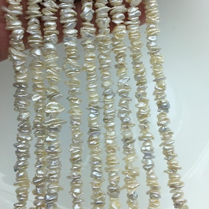 May include: Strands of irregular, off-white freshwater pearls. The pearls have a natural, organic shape and a subtle luster. The strands are held together, creating a cascading effect. The pearls vary in size and shape, adding to their unique appeal.