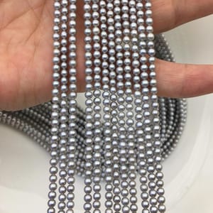 Puede incluir: Múltiples hebras de pequeñas perlas grises y redondas. Las perlas están ensartadas, creando líneas paralelas. Las perlas tienen un brillo sutil, reflejando la luz. El fondo es de un color suave y neutro, resaltando las perlas.