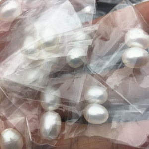 May include: A close-up of a pile of white pearls in clear plastic bags. The pearls are various sizes and shapes.